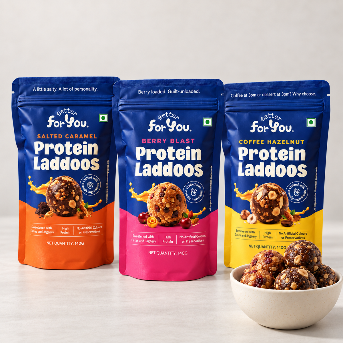 Three stand-up pouches of Better For You Protein Laddoos in Salted Caramel, Berry Blast, and Coffee Hazelnut flavors, displayed next to a white bowl filled with the protein laddoos on a light gray background.